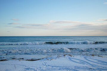Obraz premium A serene scene of a snowy Pacific coastline with black volcanic sand covered in ice, featuring gentle waves lapping at the shore.