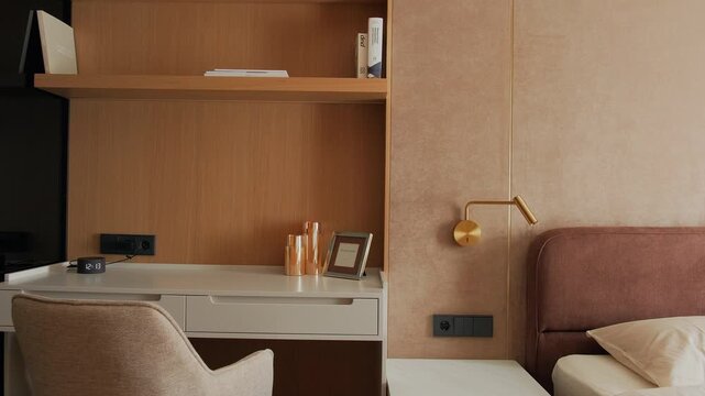 Modern bedroom interior with integrated workspace featuring desk, shelving and upholstered chair. Cozy sleeping area with soft bed, warm lighting and wooden wall panels creating a calm and functional