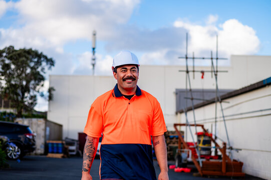 A smiling construction worker in a bright orange uniform walks through an outdoor job site