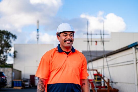 A cheerful man in high-visibility clothing stands at a construction site, smiling widely