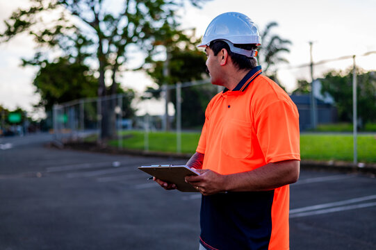 A construction worker in a high-visibility shirt surveys the site with a clipboard