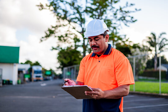 Worker in bright uniform checks details on clipboard at construction site in daylight hours
