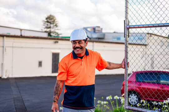 A cheerful construction worker in orange and navy shirt opens a gate at a work site