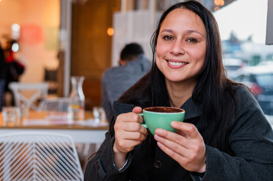 Woman holding a cup of coffee seated at the cafe table smiling