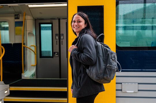 Woman waits at the train door in Wellington, New Zealand, carrying a backpack and smiling