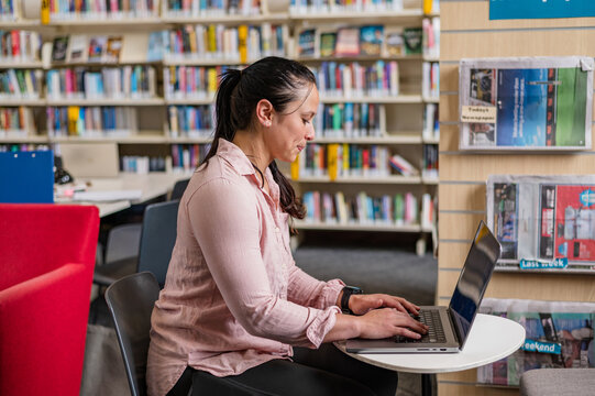Individual sits at a table typing on a laptop in a library filled with books