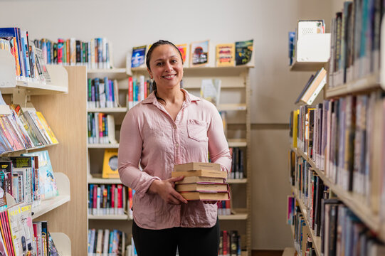 Person inside library poses with books in hands while standing between shelves of books