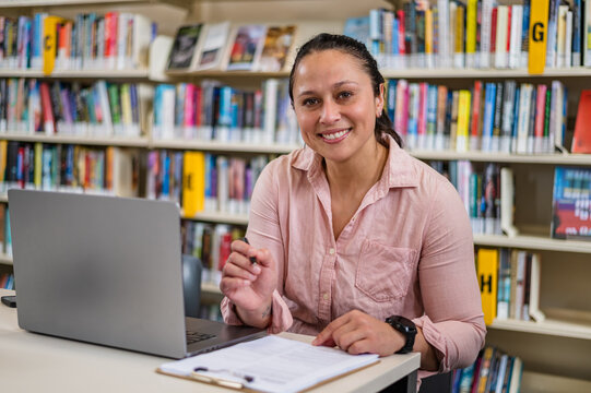 Woman sits at table with laptop and notes in library