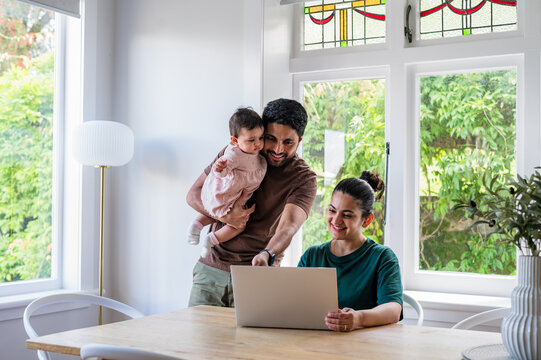 Man holds baby while woman looks at laptop on the table inside house