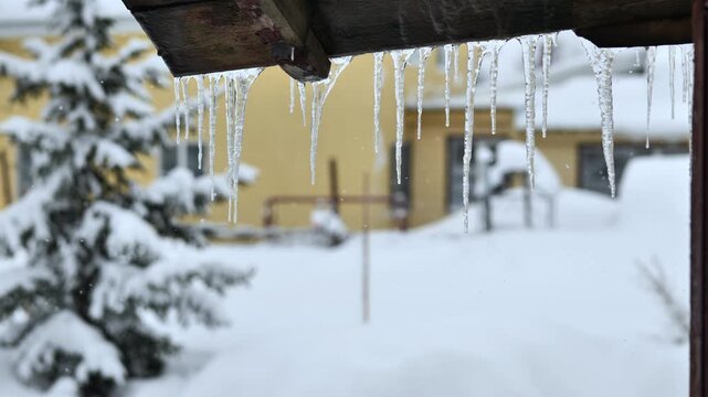 Icicles hanging from a wooden roof in a snowy winter landscape outdoors