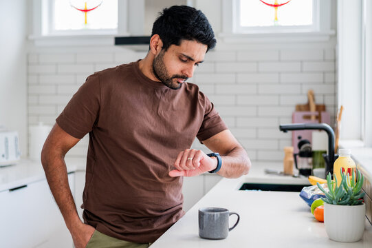 Indian man standing beside the kitchen counter looking at his smartwatch