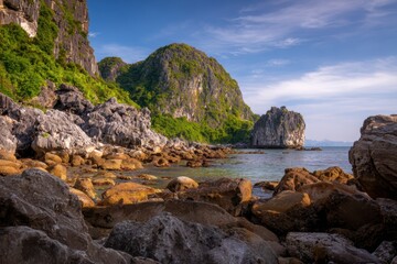 Fototapeta premium 日没時に水辺に緑の丘がある岩だらけの海岸線