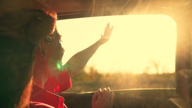 Teenage girl traveling by car. Young passenger catches wind from car window with hands. Beautiful female student drives towards sun. Family trip. Family vacation. People traveling. Family, travel, sun