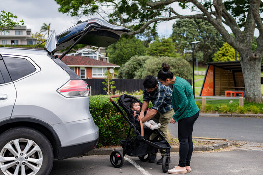 Parents buckling baby into stroller out of the car to prepare for a walk in the park