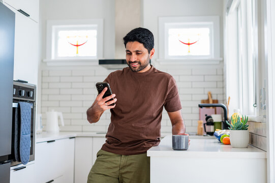 Man enjoys his time in the kitchen by checking his phone while having a drink