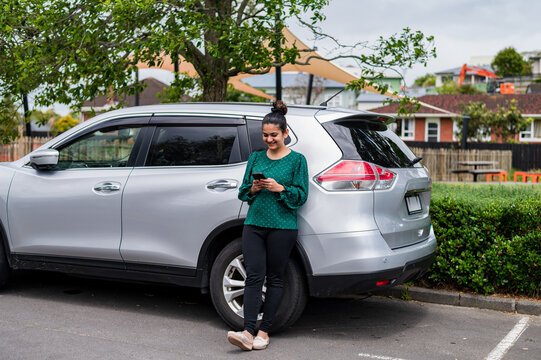Woman stands beside a silver SUV in a parking lot while looking at her phone