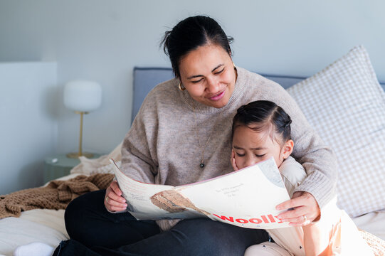 Niuean mum reading a story to her daughter while seated on the bed