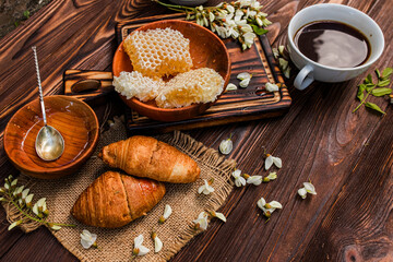 Fototapeta premium Blooming tree flowers and honeycomb with croissants and a cup of coffee on a wooden table