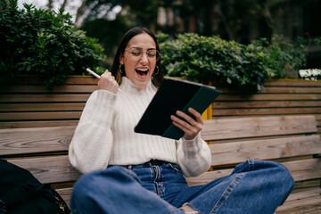 Overjoyed female designer rejoicing success while working on digital tablet outdoors, young woman...