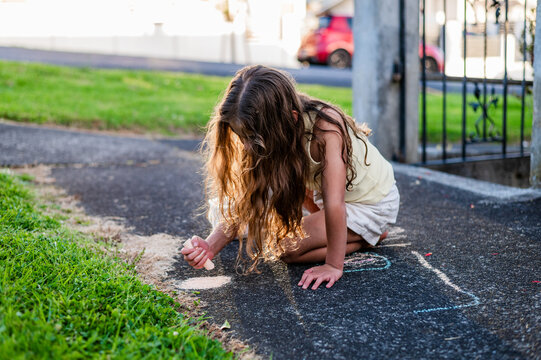 Young girl with long hair playing with chalk on the paved path outdoors