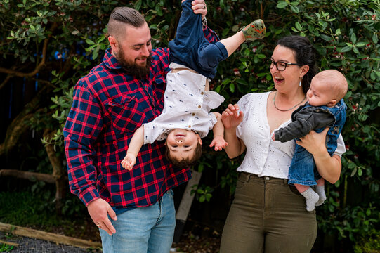 Dad holding toddler son upside down while mum carries baby boy outdoors