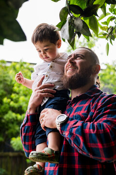 Man in red plaid shirt carrying toddler son on his shoulders outdoors