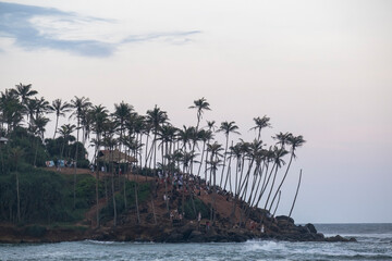 8.12.2025. Mirissa, Sri Lanka. Crowds of tourists gathered at Coconut Tree Hill in Mirissa, Sri Lanka, at sunset. Famous tropical viewpoint with palm trees and many people during golden hour.