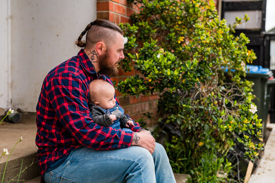 Father in red plaid shirt seated on concrete steps holding baby boy