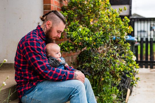 Father in red plaid shirt seated on concrete steps holding baby boy