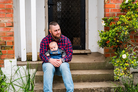 Father in red plaid shirt seated on concrete steps holding baby boy