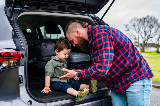 Father leaning forward towards son seated on car boot