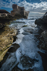 Naklejka premium Dark Coastal Channel Beneath Overhanging Coquina Rock and Surf