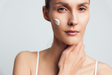 Young woman with clear skin applying moisturizing cream on cheek, natural look, soft lighting,...