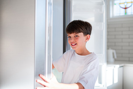 Smiling young boy opening refrigerator in bright modern kitchen in New Zealand