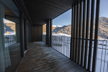 Fototapeta premium A spacious wooden balcony with vertical slatted screens faces the Dolomites in northern Italy as late afternoon light casts long shadows on the deck in winter.