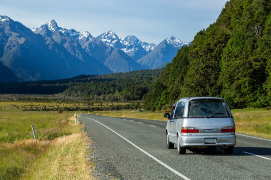 Silver minivan vehicle driving down road with snow-capped mountains in background