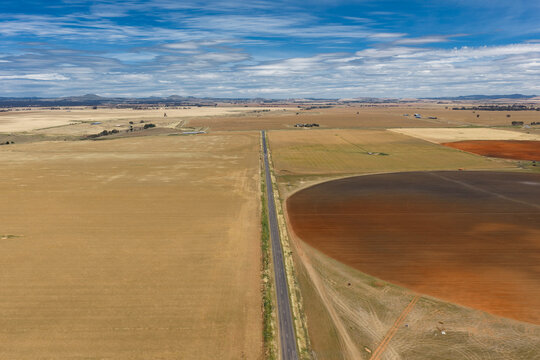 Aerial view of ploughed circular paddock alongside a country road under a blue sky