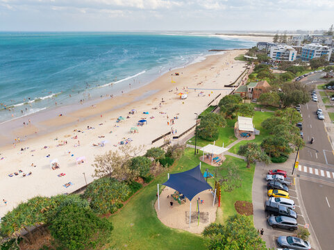 Distant aerial view of people on a sandy beach alongside a coastal parkland and carpark