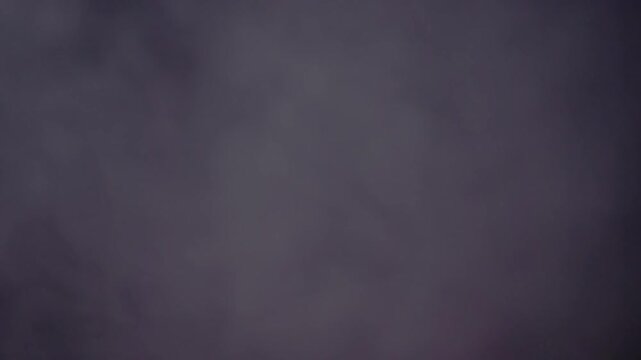 Thick plumes of dark purple smoke drift slowly across the frame creating a moody texture. Concept of mystery, horror atmosphere, abstract background, and dramatic cinematic effects.