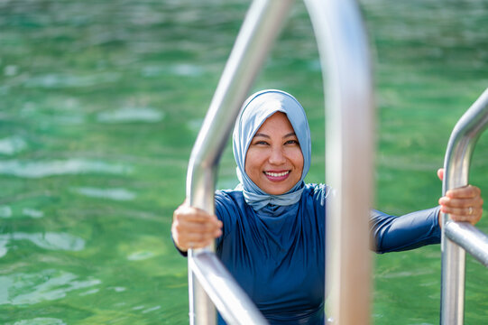 Filipina woman in a light blue headscarf holding on to metal handrail getting out of ocean pool