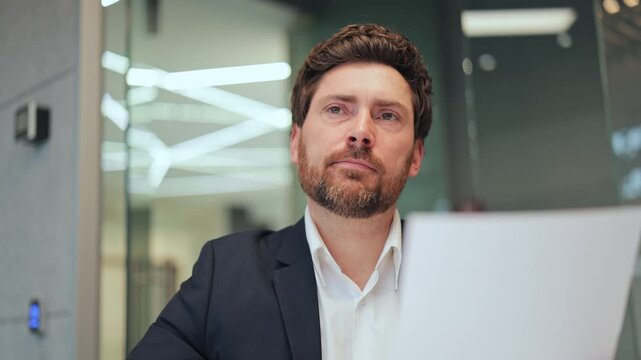 Focused business professional examining important document. Face shows serious contemplation and concern while looking up, reflecting on information in modern office.