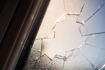 smashed window with shattered glass fragments and cracked surface, showing damage from impact or vandalism on a building exterior