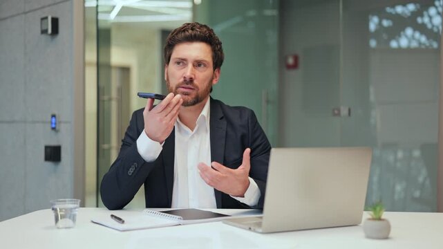 Focused professional communicates important business message using smartphone voice assistant in modern office. Expresses confidence and efficiency, representing digital communication and productivity