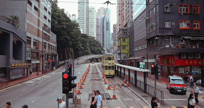Iconic double-decker tram and red taxi on busy Hong Kong street. Urban skyscrapers, pedestrians, and traffic lights. High-density metropolitan landscape. Hong Kong, 15 Apr 2025