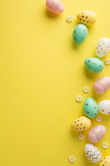Obraz na płótnie Canvas Happy Easter vertical composition with pastel decorated egg and small daisies on a bright yellow background conveying spring joy and festive decoration
