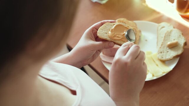 Woman spreads with teaspoon sauce on piece of white loaf. Person applies liquid aromatic spread on toast during sandwich and breakfast preparation.