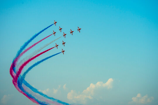 Red Arrows aerobatic team performing a dramatic vertical loop with red, white, and blue smoke trails against a clear sky.