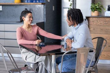 Fototapeta premium African American couple smiling, reaching across glossy black table at cafe with blue smartphone