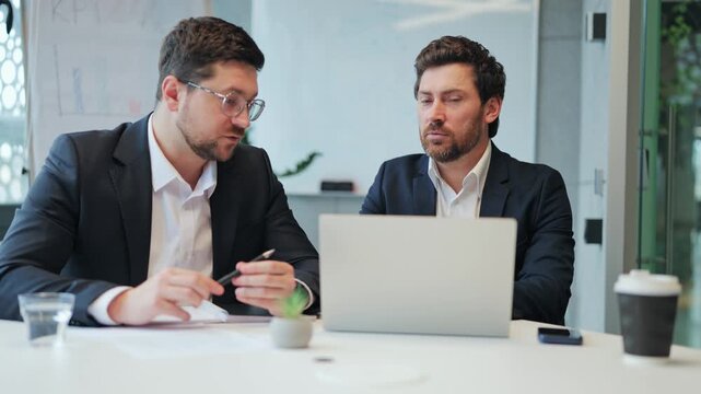 Professional colleagues engage in focused business meeting, discussing strategy and reviewing documents. Serious, determined expressions reflect dedication to work in modern office environment.