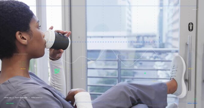 Woman in scrubs by sliding glass door, lifting coffee cup, sipping, taking break, showing bandage